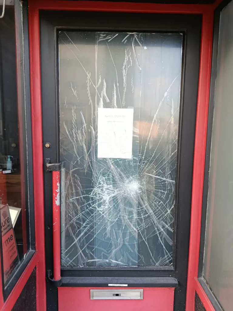 Porte d'entrée vitrée d'un commerce entièrement brisée suite à un acte de vandalisme ou une effraction, nécessitant une intervention d'urgence.